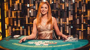 Studio dealer langsung dengan monitor multi-sudut, dealer profesional di balik meja blackjack, dan antarmuka taruhan di layar pemain